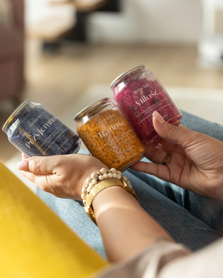 Trzy puszki soli do kąpieli Herbal SPA trzymane w dłoniach